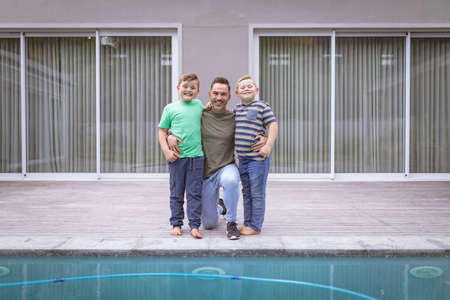 Portrait of caucasian father and two sons holding hands smiling while standing near the pool....