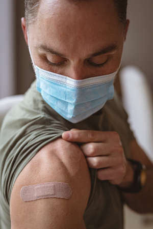 Caucasian man wearing face mask showing his vaccinated shoulder at home. vaccination for prevention...