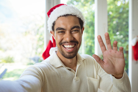 Portrait of happy biracial man in santa hat making christmas video call. christmas, festivity and communication technology.の写真素材