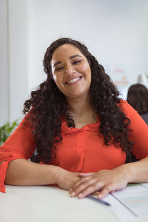Smiling biracial businesswoman sitting at desk making video call in modern office. business and...