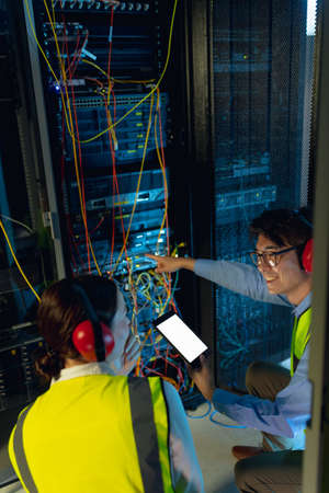 Diverse male and female engineer using digital tablet while inspecting in computer server room....