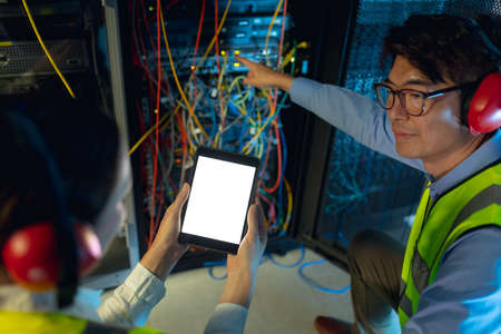 Diverse male and female engineer using digital tablet while inspecting in computer server room. database server management and maintenance conceptの写真素材