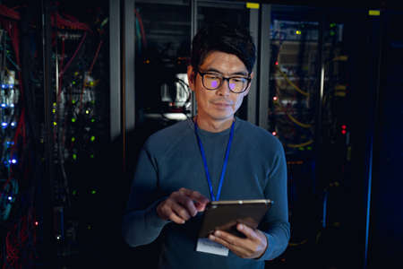 Asian male engineer using digital tablet in computer server room. database server management and maintenance conceptの写真素材
