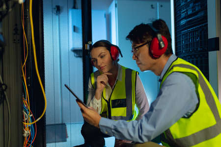 Diverse male and female engineer using digital tablet while inspecting in computer server room....