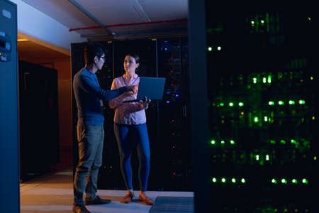 Diverse male and female engineers using laptop in computer server room. database server management and maintenance conceptの写真素材