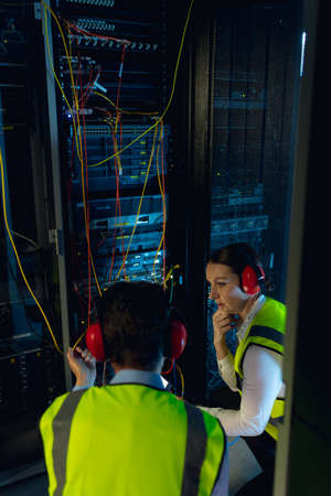 Diverse male and female engineers discussing together while inspecting iin computer server room. database server management and maintenance conceptの写真素材