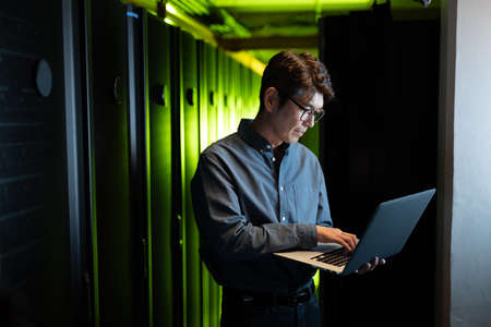Asian male engineer using laptop in computer server room. database server management and maintenance conceptの写真素材