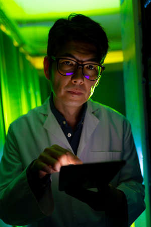 Portrait of asian male engineer wearing an apron using digital tablet in computer server room....