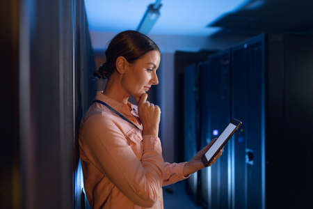Thoughtful caucasian female engineer using digital tablet in computer server room. database server management and maintenance conceptの写真素材