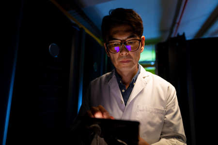 Asian male engineer wearing an apron using digital tablet in computer server room. database server management and maintenance conceptの写真素材