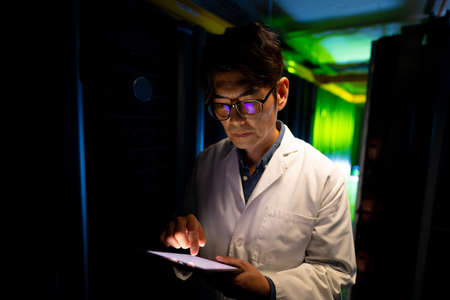 Asian male engineer wearing an apron using digital tablet in computer server room. database server...