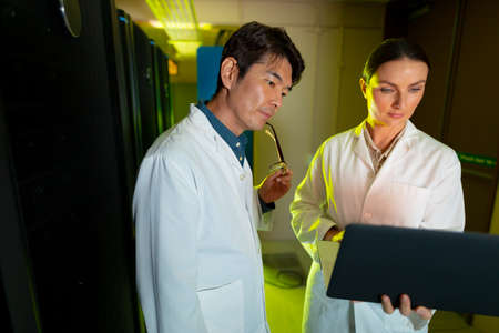 Diverse male and female engineers wearing aprons using laptop while inspecting in server room....