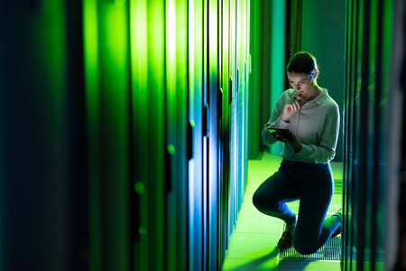 Caucasian female engineer using digital tablet while inspecting in computer server room. database server management and maintenance conceptの写真素材