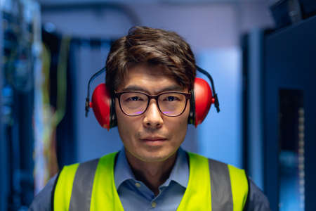 Portrait of asian male engineer wearing ear plugs in computer server room. database server management and maintenance conceptの写真素材