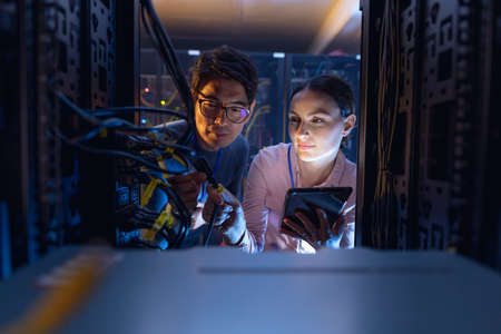 Diverse male and female engineers with digital tablet inspecting the server in computer server room. database server management and maintenance conceptの写真素材