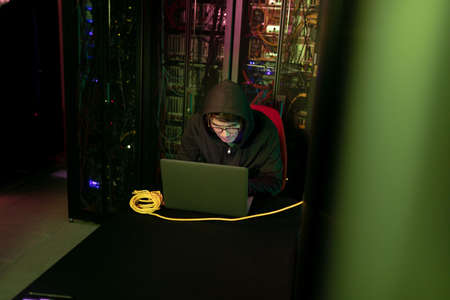 Asian male hacker using a laptop in computer server room. cyber crime and hacking conceptの写真素材