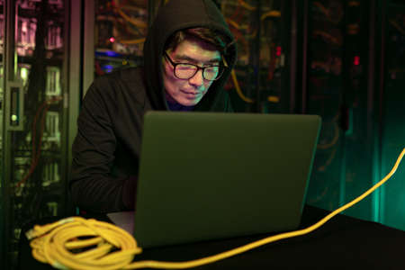 Asian male hacker using a laptop in computer server room. cyber crime and hacking conceptの写真素材