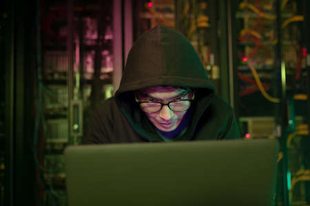 Asian male hacker using a laptop in computer server room. cyber crime and hacking conceptの写真素材