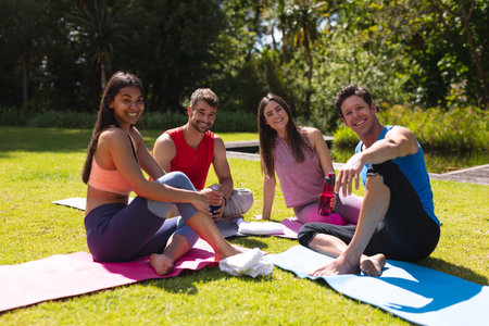 Portrait of smiling men and women sitting on exercise mats after workout in park. yoga, healthy lifestyle and friendship.の写真素材