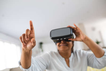 African american senior woman pointing while wearing virtual reality simulator at home, copy space....