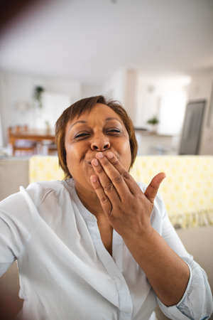 Happy african american senior woman blowing kiss during video call at home. lifestyle and...