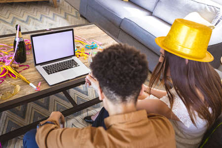 Biracial couple enjoying virtual party through video call on laptop with copy space. celebration, lifestyle and telecommunications.の写真素材
