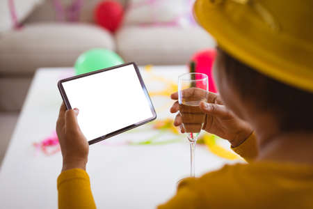Senior woman video calling through tablet pc while enjoying champagne in party at home, copy space. lifestyle, celebration, young at heart and wireless technology.の写真素材