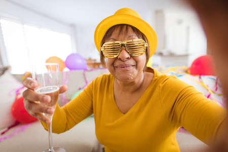 Senior woman in shutter glasses making video call while enjoying champagne during party at home. lifestyle, celebration, young at heart and communication.の写真素材