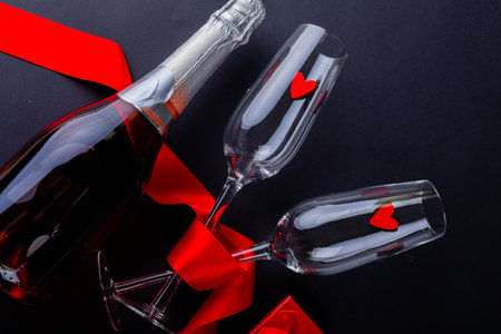 Heart shapes in flutes with red ribbon by champagne bottle over black background with copy space. love and valentine celebration.の写真素材