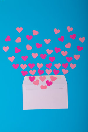 Open white envelope with scattered peach and pink colored heart shapes on blue background. love,...