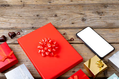 Blank screen on mobile phone with copy space arranged by gift boxes on wooden table. technology, love and valentine.の写真素材