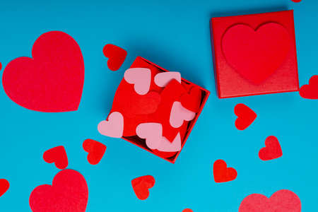 Overhead view of gift box with red and pink paper hearts scattered on blue background. love, valentine gift and copy space.の写真素材