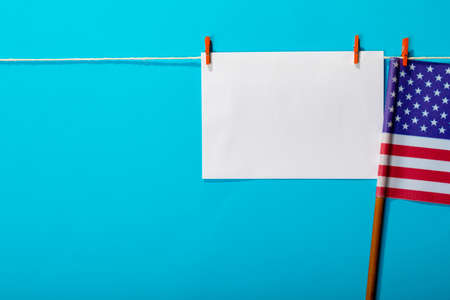 Blank paper with copy space hanging by america flag hanging from clothesline on blue background. patriotism and identity with copy space.の写真素材