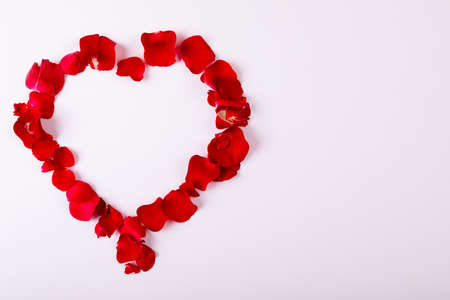 Overhead view of red rose petals arranged as heart shape with copy space on white background. love and valentine symbol.の写真素材