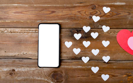 Smartphone with blank screen showing copy space by white heart shapes on wooden table. technology, love and valentine.の写真素材