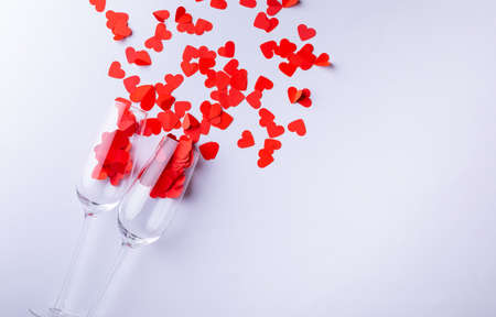 Champagne flutes with red heart shapes scattered by copy space over white background. love and valentine.の写真素材