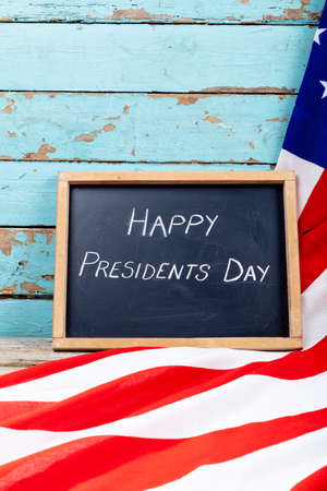 Happy presidents day text on writing slate with usa flag on blue wooden table with copy space. patriotism and identity, celebration.の写真素材