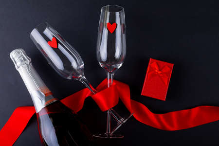 Champagne flutes tied with red ribbon by gift box and bottle on gray background, copy space....