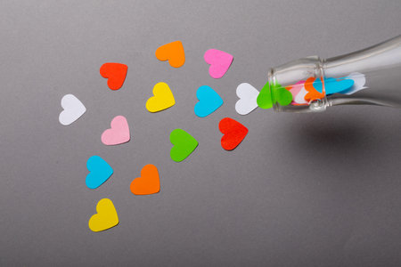 Glass bottle pouring colorful heart shaped papers on gray background with copy space. valentine's day and love concept.の写真素材