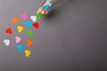 Bottle pouring colorful heart shaped papers over gray background with copy space. valentine's...