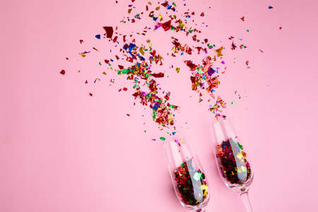 Multi colored confetti and champagne flutes isolated against pink background, copy space. party and celebration.の写真素材