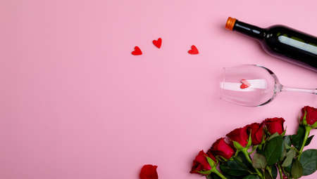 Overhead view of wine bottle and glass with red roses isolated on pink background, copy space. valentine's day, flower, drink and love concept.の写真素材