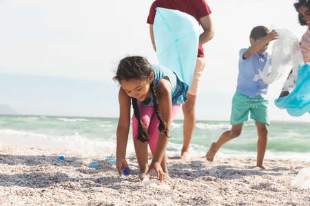 Biracial girl collecting plastic garbage on sand at beach with family during sunny day. lifestyle and environmentalism.の写真素材