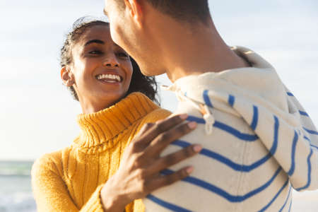 Happy biracial young woman looking boyfriend while embracing him at beach on sunny day. lifestyle, love and weekend.の写真素材