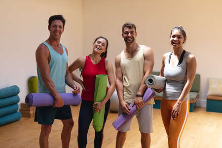 Portrait of multiracial happy men and women with mats standing in yoga studio. healthy lifestyle and fitness.の写真素材