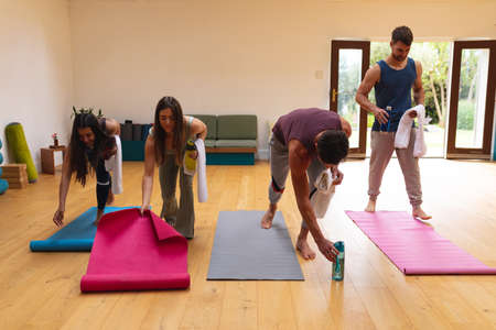 Multiracial men and women arranging exercise mats on hardwood floor in yoga studio. fitness, yoga...