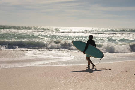 Full length of biracial senior man carrying surfboard walking towards waves in sea at beach. water...