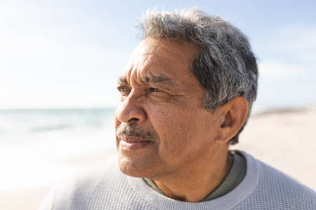Close-up of retired biracial senior man looking away while thinking at beach during sunny day....