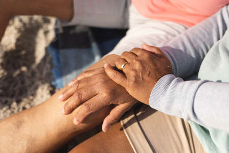 Midsection of biracial senior woman with hands on man's knee sitting at beach during sunny day. lifestyle, love and weekend.の写真素材