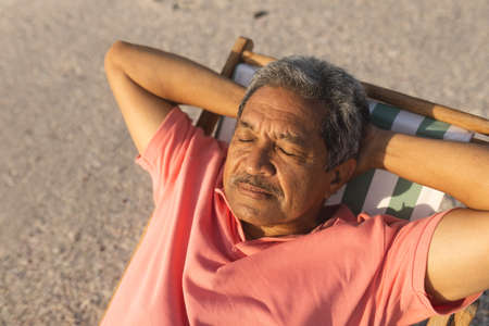 High angle view of retired senior biracial man sleeping with hands behind head on chair at beach. lifestyle and weekend.の写真素材